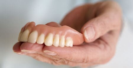 closeup of womans hand holding a teeth denture